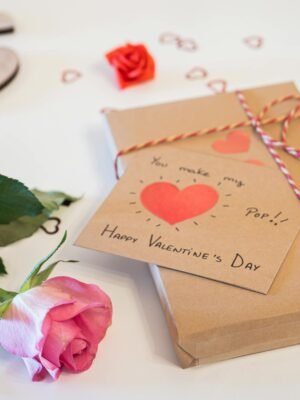 A charming Valentine's Day gift setup with a pink rose, a heart card, and decorative elements on a white background.