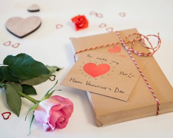 A charming Valentine's Day gift setup with a pink rose, a heart card, and decorative elements on a white background.