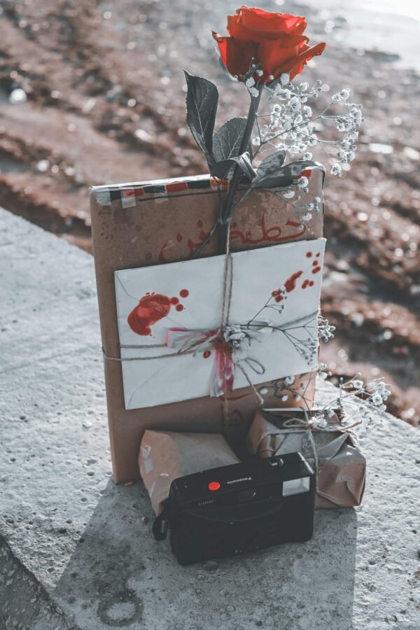 Close-up of a romantic gift set with a red rose, vintage camera, and wrapped items outdoors.